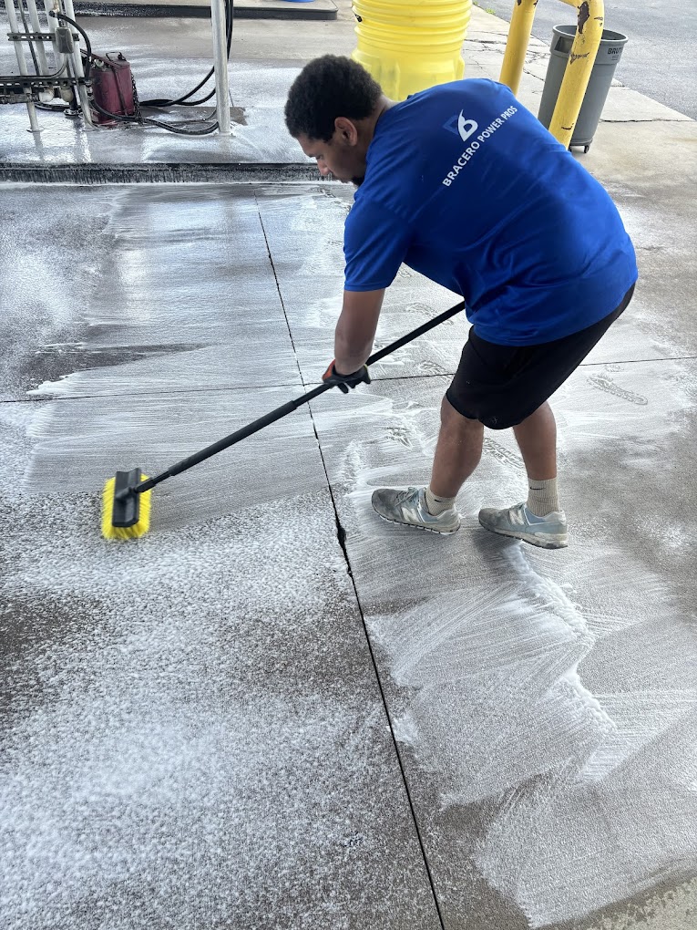 Bracero Power Pros technician scrubbing soapy concrete clean with a wide deck brush